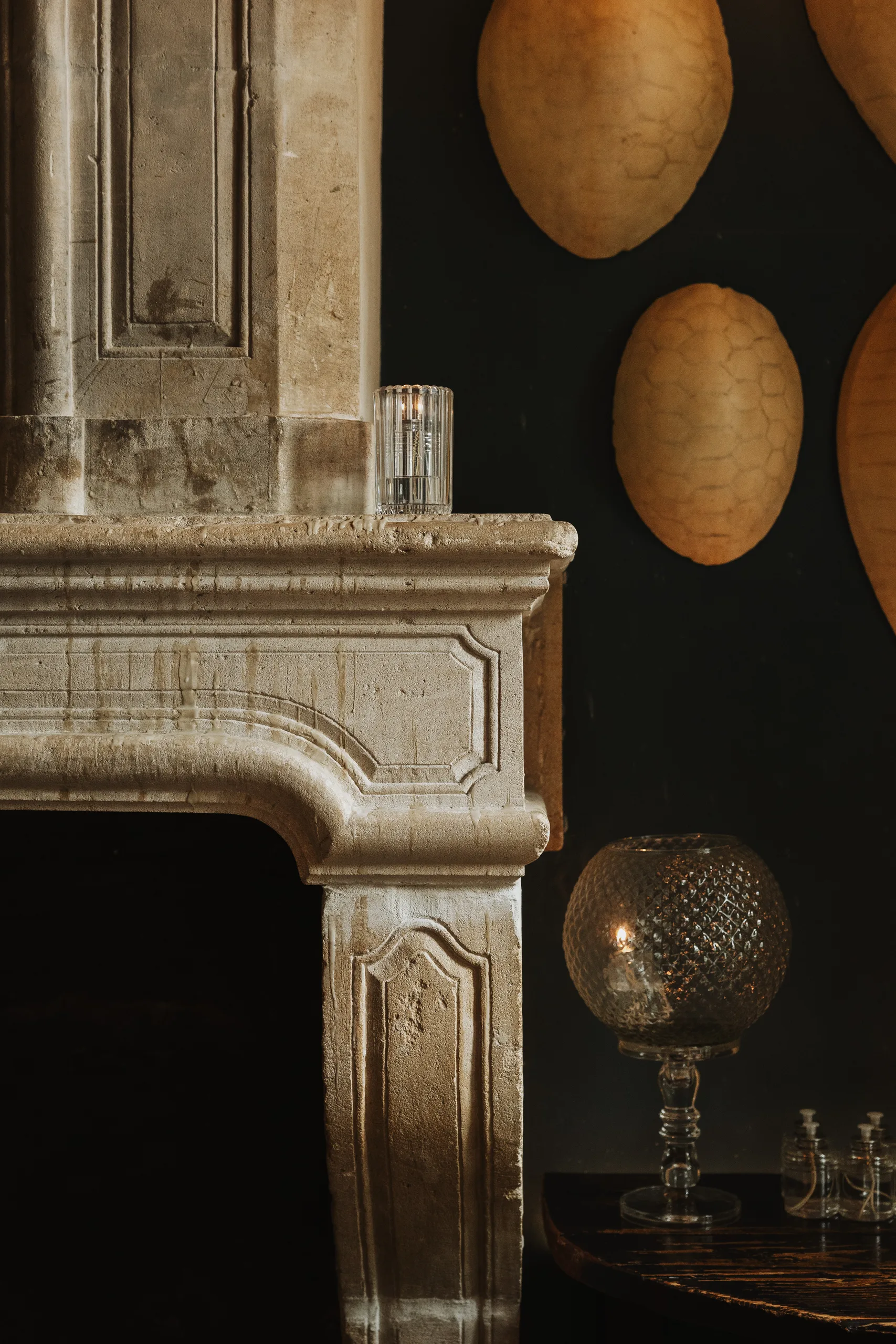 Stone fireplace mantel with oval wall shields and a glass lamp