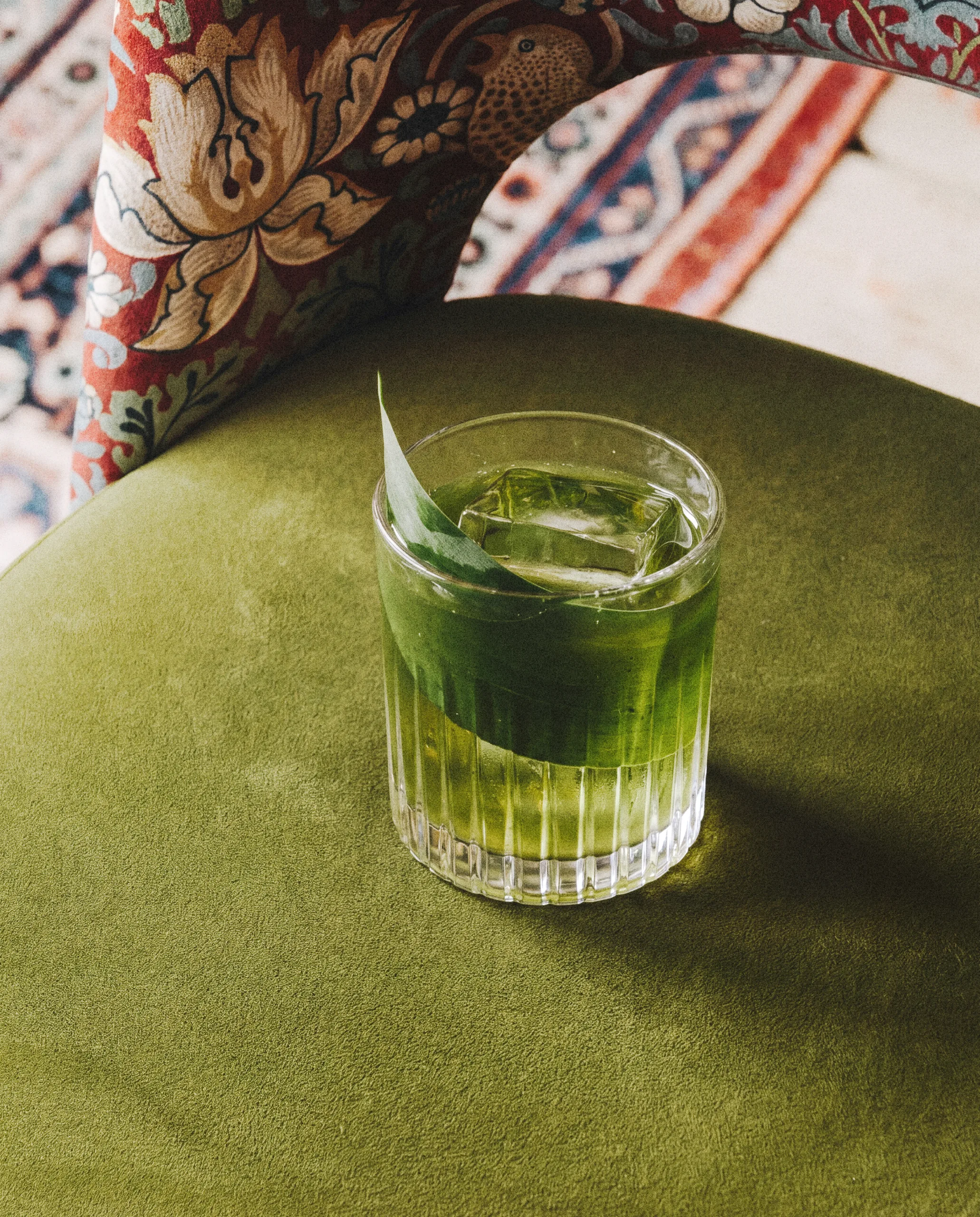 Green cocktail with a large ice cube on a velvet chair
